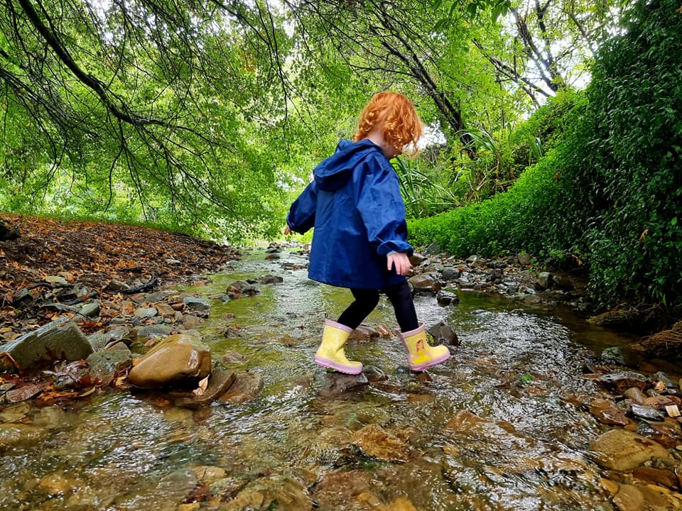 Child in yellow gum boots and a blue coat paddling in a steam for outdoor play