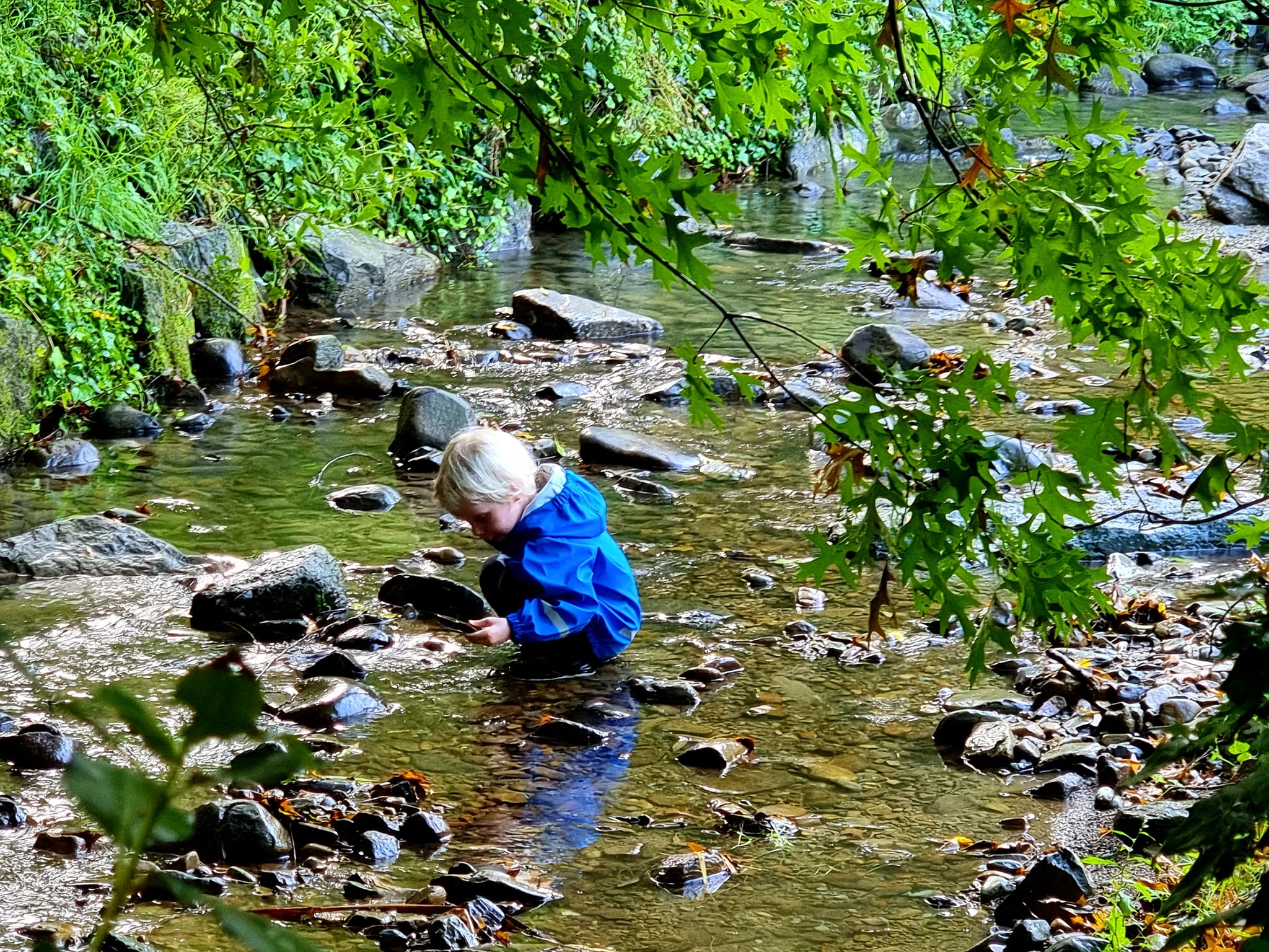 Child in a blue coat squatting in a steam for outdoor play