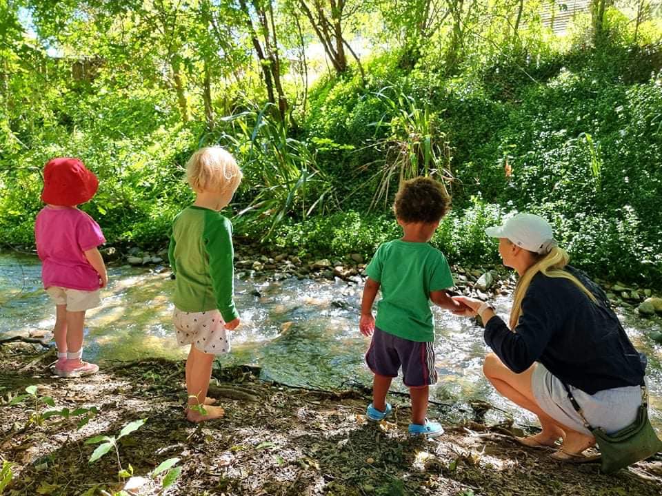 A group of three children and their carer looking into a stream during outdoor play
